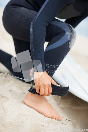 Image of Foot, ankle and strap with a surfer on the beach closeup, getting ready for sports or fitness training. Hands, hobby and tie with a person on the sand at the coast for safety during an exercise hobby