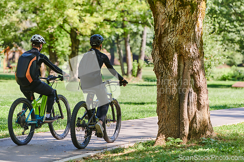 Image of A blissful couple, adorned in professional cycling gear, enjoys a romantic bicycle ride through a park, surrounded by modern natural attractions, radiating love and happiness