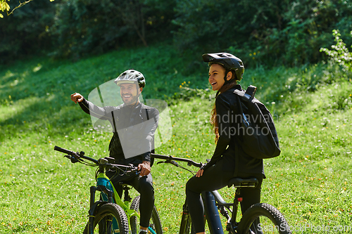 Image of A blissful couple, adorned in professional cycling gear, enjoys a romantic bicycle ride through a park, surrounded by modern natural attractions, radiating love and happiness