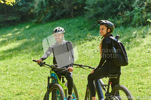 Image of A blissful couple, adorned in professional cycling gear, enjoys a romantic bicycle ride through a park, surrounded by modern natural attractions, radiating love and happiness