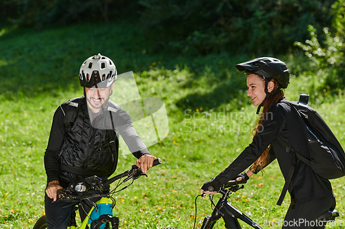 Image of A blissful couple, adorned in professional cycling gear, enjoys a romantic bicycle ride through a park, surrounded by modern natural attractions, radiating love and happiness