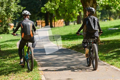 Image of A blissful couple, adorned in professional cycling gear, enjoys a romantic bicycle ride through a park, surrounded by modern natural attractions, radiating love and happiness