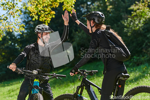 Image of A sweet couple, adorned in cycling gear, rides their bicycles, their hands interlocked in a romantic embrace, capturing the essence of love, adventure, and joy on a sunlit path