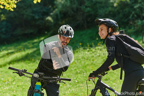 Image of A blissful couple, adorned in professional cycling gear, enjoys a romantic bicycle ride through a park, surrounded by modern natural attractions, radiating love and happiness