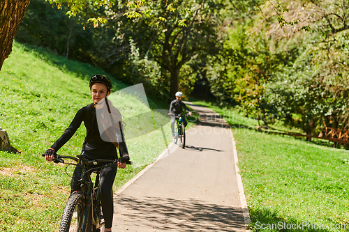 Image of A blissful couple, adorned in professional cycling gear, enjoys a romantic bicycle ride through a park, surrounded by modern natural attractions, radiating love and happiness