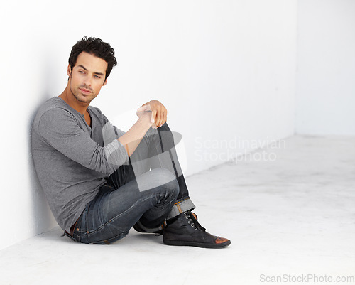 Image of Handsome, fashion and young man by a white wall with casual, cool and trendy outfit. Attractive, confidence and serious male model from Canada sitting on floor with edgy style for aesthetic.