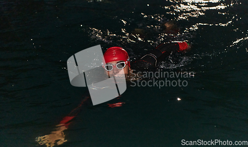 Image of A determined professional triathlete undergoes rigorous night time training in cold waters, showcasing dedication and resilience in preparation for an upcoming triathlon swim competition