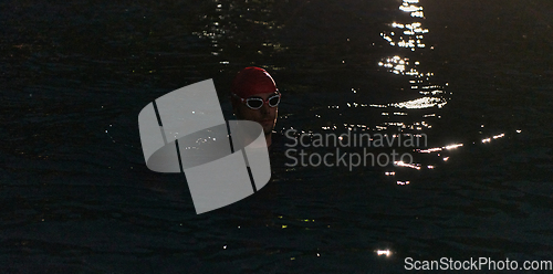 Image of A determined professional triathlete undergoes rigorous night time training in cold waters, showcasing dedication and resilience in preparation for an upcoming triathlon swim competition