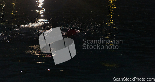 Image of A determined professional triathlete undergoes rigorous night time training in cold waters, showcasing dedication and resilience in preparation for an upcoming triathlon swim competition