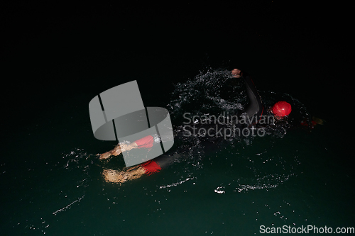 Image of A determined professional triathlete undergoes rigorous night time training in cold waters, showcasing dedication and resilience in preparation for an upcoming triathlon swim competition