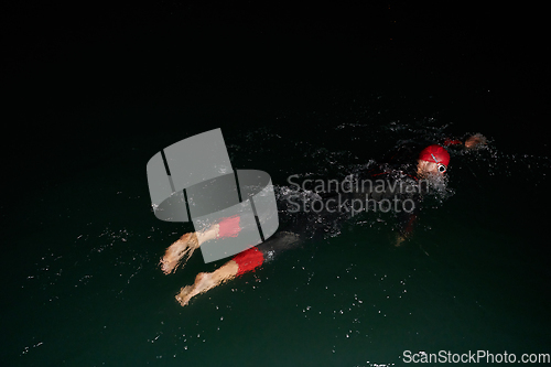 Image of A determined professional triathlete undergoes rigorous night time training in cold waters, showcasing dedication and resilience in preparation for an upcoming triathlon swim competition