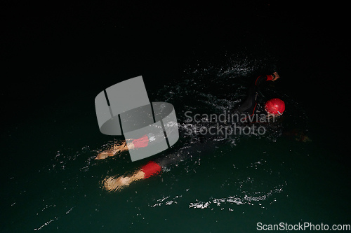 Image of A determined professional triathlete undergoes rigorous night time training in cold waters, showcasing dedication and resilience in preparation for an upcoming triathlon swim competition