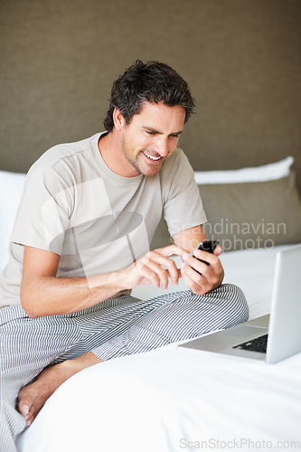 Image of Phone, social media and laptop with a man in the bedroom of his home to relax on weekend time off. Tech, communication and person sitting on a bed while streaming a movie or series for entertainment