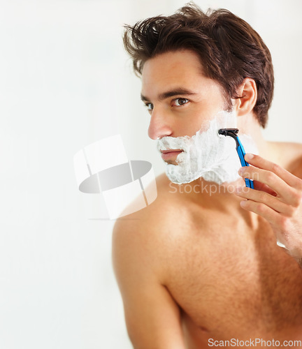 Image of Skincare, shaving and razor with a man in the bathroom of his home for grooming or morning routine. Face, beauty and foam with a young person in his apartment to shave his beard for hair removal