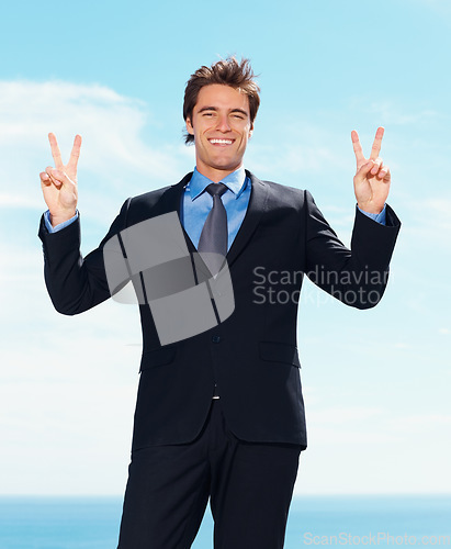 Image of Portrait, smile and peace sign with a business man outdoor on a blue sky background for success or motivation. Corporate, professional and hand gesture with a happy young employee in a formal suit
