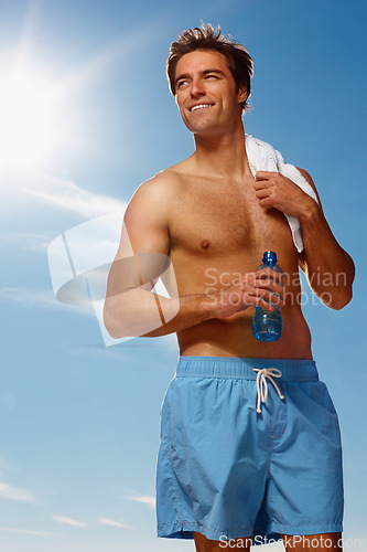 Image of Man, shirtless and water bottle or towel for workout with health body, fitness or happiness on vacation. Model, smile or natural glow with drink for hydration or post exercise in sunshine with shorts