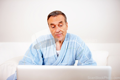 Image of Gown, morning and mature man on laptop reading email, social media or streaming subscription on sofa. Internet search, couch and senior person in bathrobe on computer, website or networking in home.