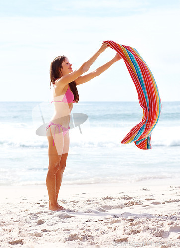 Image of Woman, happy and towel on sand at beach for relax, sun tan and sunshine with bikini outdoor in summer. Person, smile and swimsuit by ocean with swimming, peace and wellness on holiday or vacation