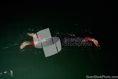 Image of A determined professional triathlete undergoes rigorous night time training in cold waters, showcasing dedication and resilience in preparation for an upcoming triathlon swim competition