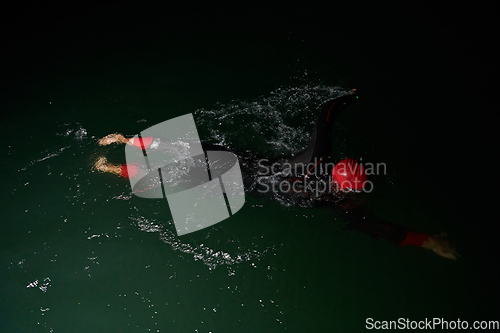 Image of A determined professional triathlete undergoes rigorous night time training in cold waters, showcasing dedication and resilience in preparation for an upcoming triathlon swim competition