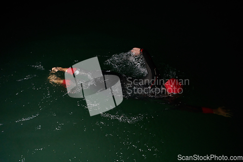 Image of A determined professional triathlete undergoes rigorous night time training in cold waters, showcasing dedication and resilience in preparation for an upcoming triathlon swim competition