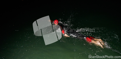 Image of A determined professional triathlete undergoes rigorous night time training in cold waters, showcasing dedication and resilience in preparation for an upcoming triathlon swim competition