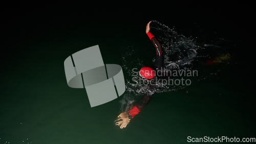 Image of A determined professional triathlete undergoes rigorous night time training in cold waters, showcasing dedication and resilience in preparation for an upcoming triathlon swim competition