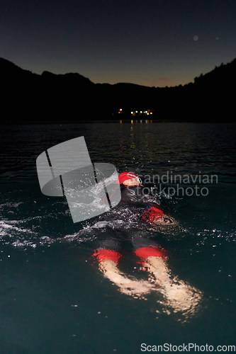 Image of A determined professional triathlete undergoes rigorous night time training in cold waters, showcasing dedication and resilience in preparation for an upcoming triathlon swim competition