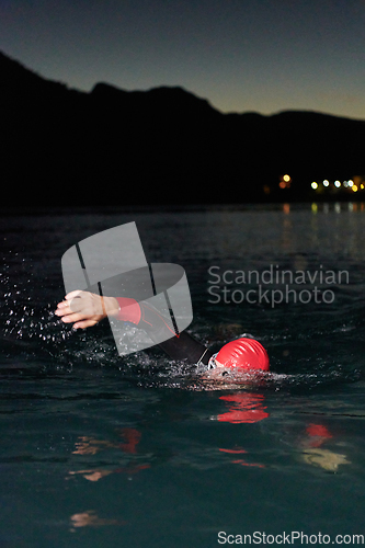 Image of A determined professional triathlete undergoes rigorous night time training in cold waters, showcasing dedication and resilience in preparation for an upcoming triathlon swim competition