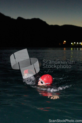 Image of A determined professional triathlete undergoes rigorous night time training in cold waters, showcasing dedication and resilience in preparation for an upcoming triathlon swim competition