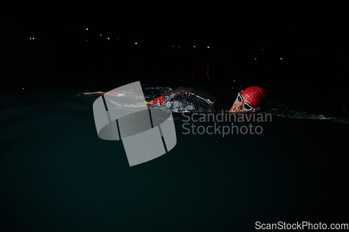 Image of A determined professional triathlete undergoes rigorous night time training in cold waters, showcasing dedication and resilience in preparation for an upcoming triathlon swim competition