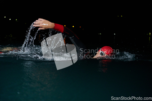 Image of A determined professional triathlete undergoes rigorous night time training in cold waters, showcasing dedication and resilience in preparation for an upcoming triathlon swim competition