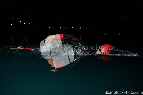 Image of A determined professional triathlete undergoes rigorous night time training in cold waters, showcasing dedication and resilience in preparation for an upcoming triathlon swim competition