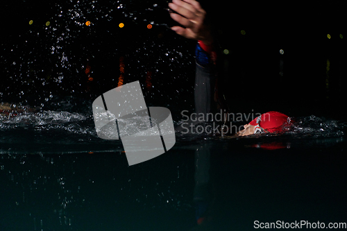 Image of A determined professional triathlete undergoes rigorous night time training in cold waters, showcasing dedication and resilience in preparation for an upcoming triathlon swim competition