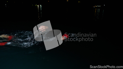 Image of A determined professional triathlete undergoes rigorous night time training in cold waters, showcasing dedication and resilience in preparation for an upcoming triathlon swim competition