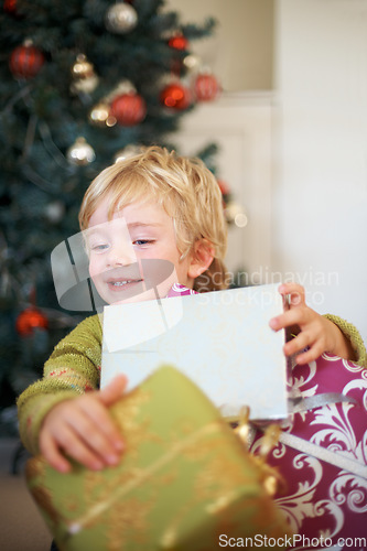 Image of Christmas, festive and a boy opening a present under a tree in the morning for celebration or tradition. Kids, gift and excitement with an adorable young child in the living room of his home