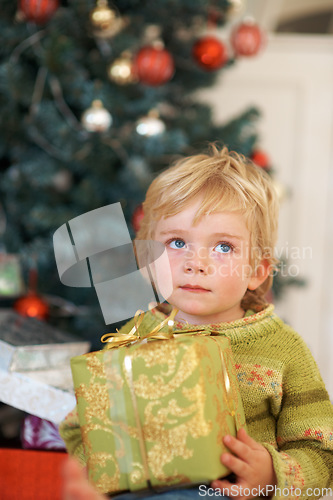 Image of Christmas, thinking and a boy opening a present under a tree in the morning for celebration or tradition. Kids, gift and wonder with an adorable young child in the living room of his home in December