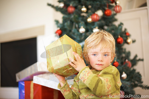 Image of Christmas, listening and a boy opening a present under a tree in the morning for celebration or tradition. Kids, gift and shaking a box with an adorable young child in the living room of his home