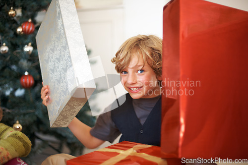 Image of Portrait, christmas and a boy opening a present under a tree in the morning for celebration or tradition. Kids, gift and excitement with a happy, young or cute child in the living room of his home