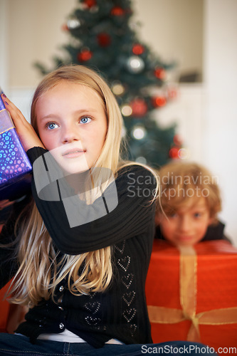 Image of Christmas, listening and a girl opening a present under a tree in the morning for celebration or tradition. Kids, gift and festive with an adorable young child in the living room of her home