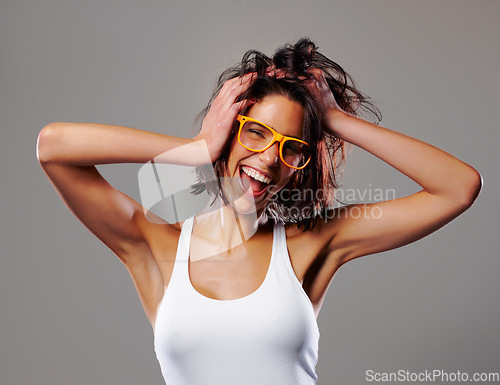 Image of Portrait, smile and crazy with a messy hair woman in studio on a gray background for silly expression. Fashion, glasses and a happy young person feeling goofy with energy, freedom or excitement