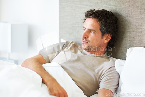 Image of Thinking, depression and man in bed with mental health crisis, disaster or broken heart in his home. Overthinking, face and person in a bedroom with anxiety, stress or frustrated by insomnia fatigue