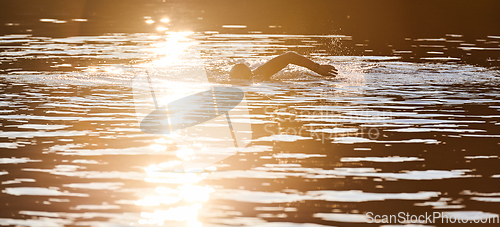 Image of Triathlon athlete swimming on lake in sunrise wearing wetsuit