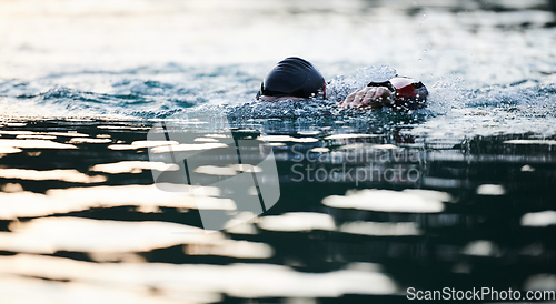 Image of Triathlon athlete swimming on lake in sunrise wearing wetsuit