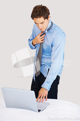 Image of Businessman, laptop and getting ready on bed for deadline, tasks or morning schedule plan at home. Man or employee working on computer while dressing tie or suit for formal business in the bedroom