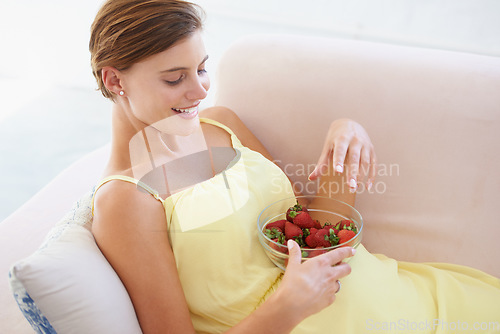 Image of Pregnant woman, eating strawberries and happy in home, alone and enjoying delicious pregnancy craving. Good mood, fruit and maternity wellness with healthy food snack and nutrition satisfaction