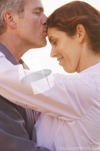 Image of Couple, forehead kiss and hug with love, respect or happiness on holiday in retirement. Mature, man and woman embrace together outdoor at sunset on vacation or show affection or gratitude in marriage