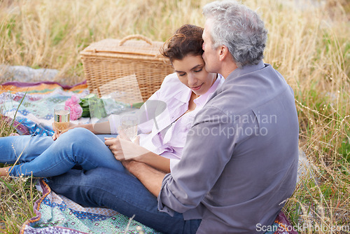 Image of Couple, kiss and relax at picnic on grass with wine, drinks and celebration on date in park. Love, man and woman with food, basket and flowers for marriage anniversary or outdoor in nature on holiday