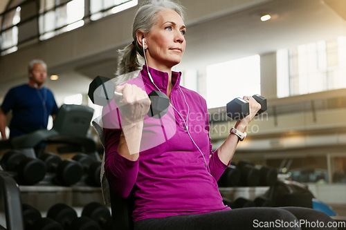 Image of Old woman, fitness and dumbbells at gym for training, wellness and cardio with earphones, music or mindset. Weightlifting, bodybuilding and senior female person at a sports center for biceps workout