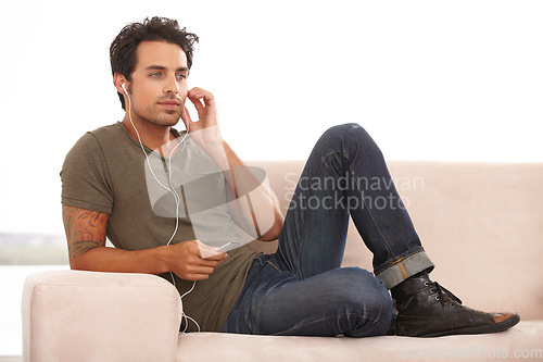 Image of Man, player or earphones on sofa and music, podcast or radio streaming for break in living room of home. Person, face or listening with technology on couch in lounge for sound, song or audio in house